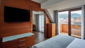 Un dormitorio moderno con un armario de madera, un televisor de pantalla plana, una cama y un balcón con vistas a la ciudad.