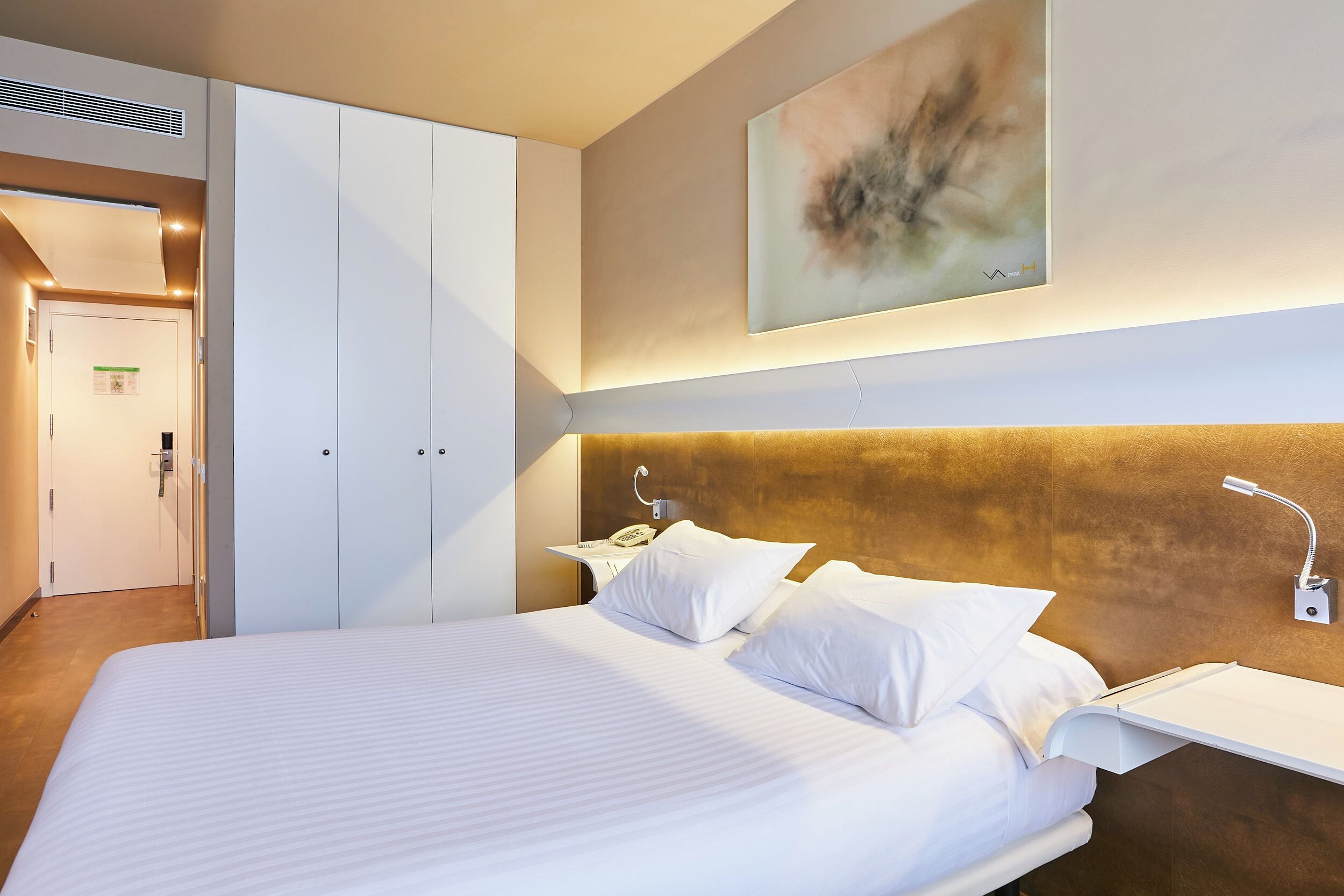 Een hotelkamer met een groot bed, nachtkastjes, een telefoon aan de muur en een schilderij boven het bed.