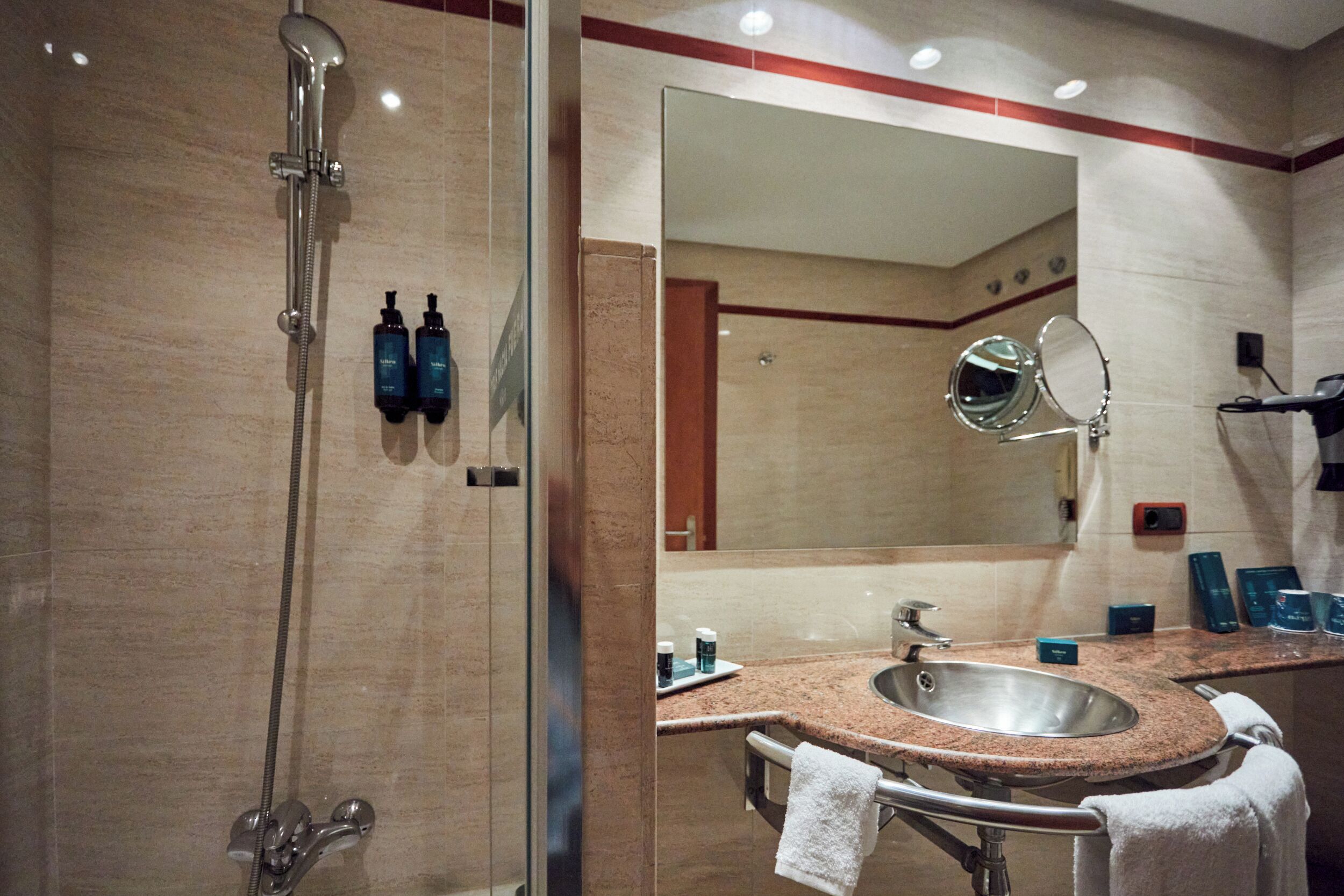 Une salle de bain avec une douche à parois de verre, un lavabo avec un miroir et des articles de toilette posés sur le comptoir.