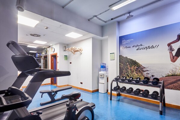 Une salle de sport équipée de matériel d’exercice, d’un distributeur d’eau et d’une affiche motivante au mur.