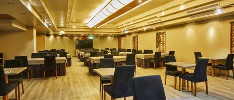 A conference room with multiple tables and chairs, a stage at the front, and a wooden floor.
