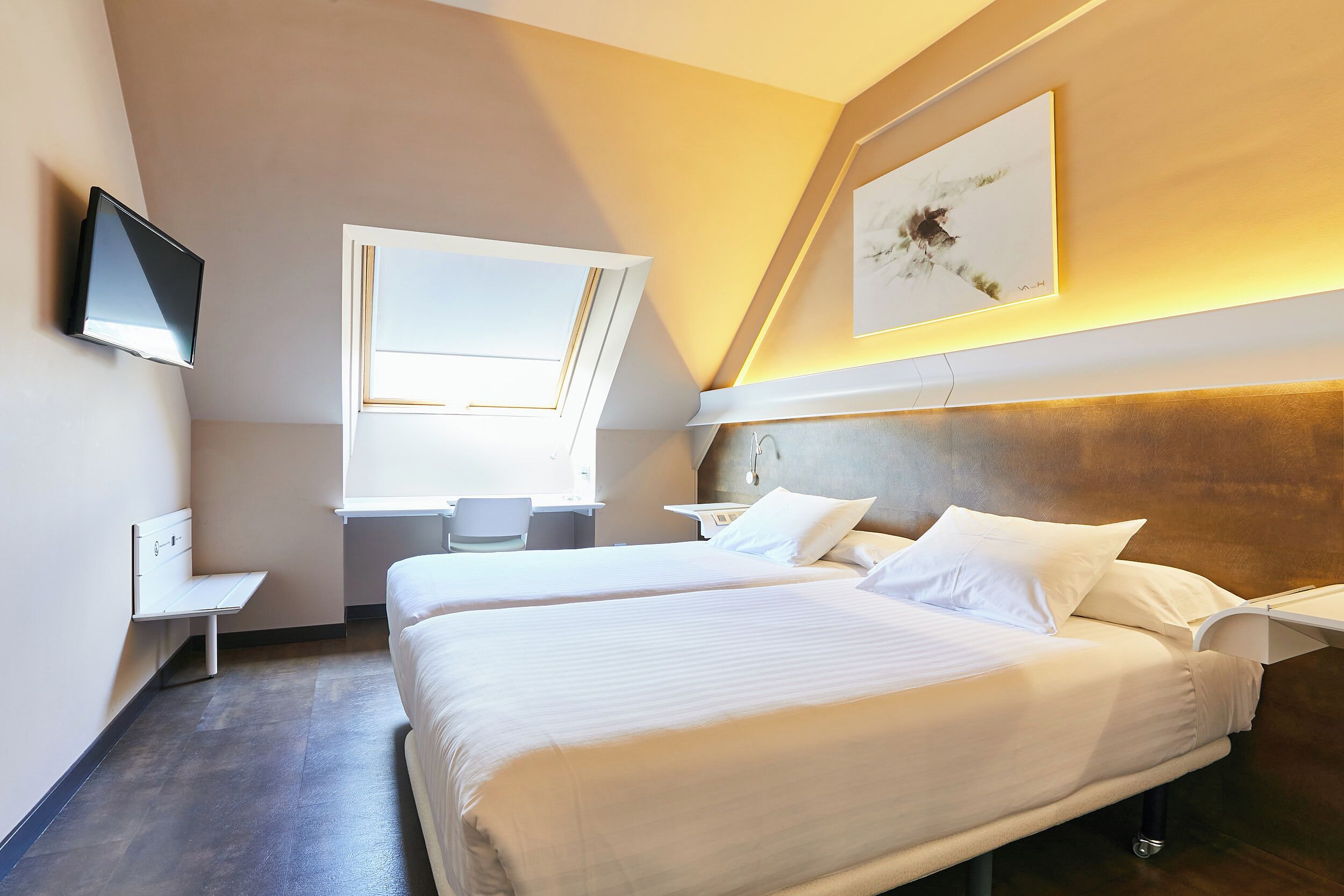 A modern hotel room with two beds, a desk, a chair, and a TV mounted on the wall.