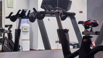 Bicicleta ergométrica numa academia, com um espelho refletindo o ambiente.