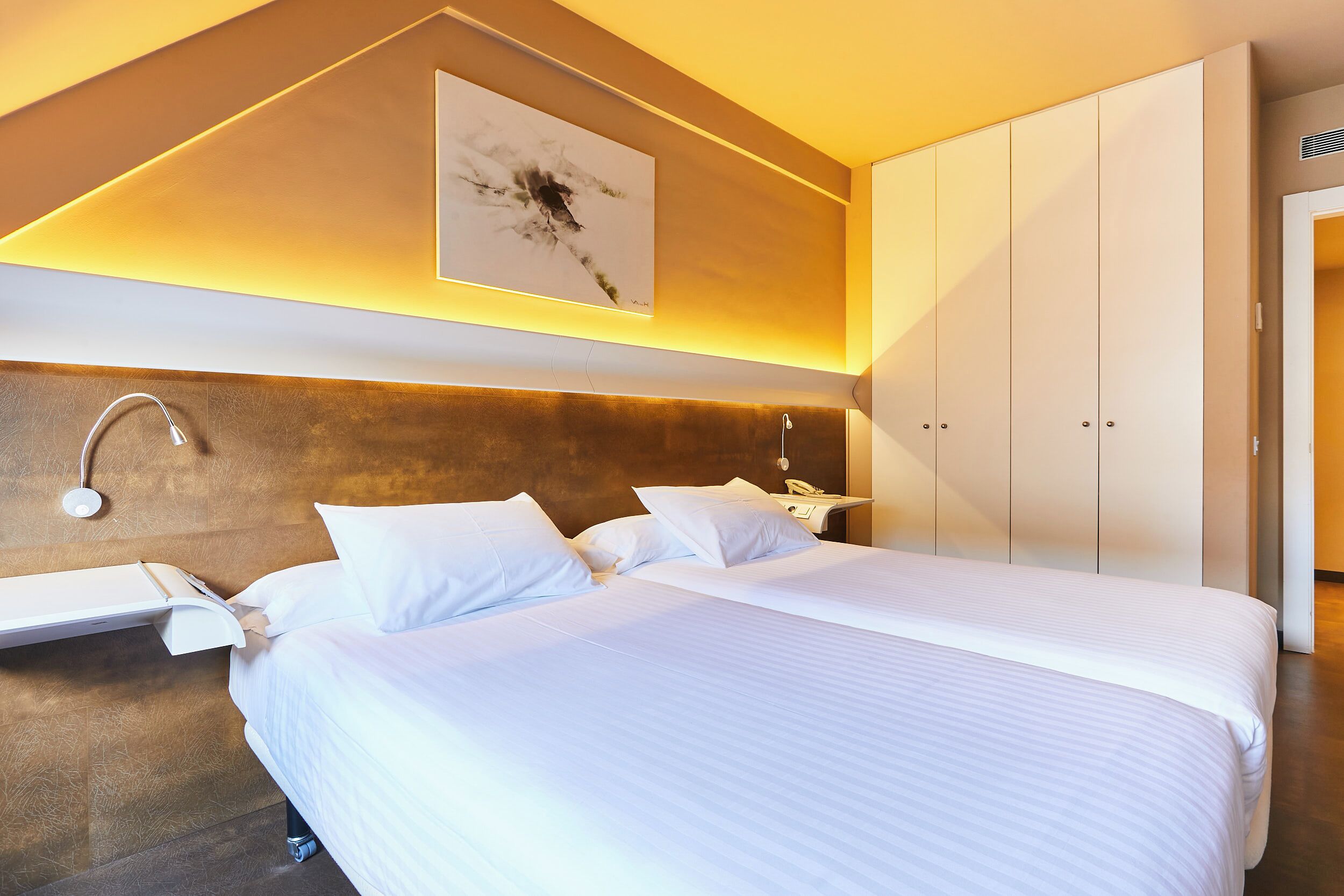 Une chambre d’hôtel moderne, dotée d’un grand lit, d’une table de chevet, d’une œuvre d’art accrochée au mur et d’armoires intégrées.