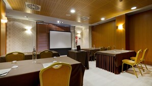 Un salón de conferencias con mesas, sillas, una pantalla de proyector y techo de madera.
