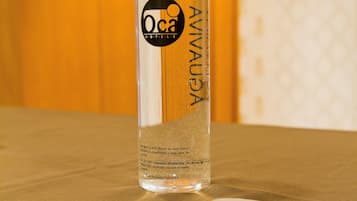 Una botella transparente con la etiqueta 'Oca' sobre una mesa de madera, con un ordenador portátil al frente.