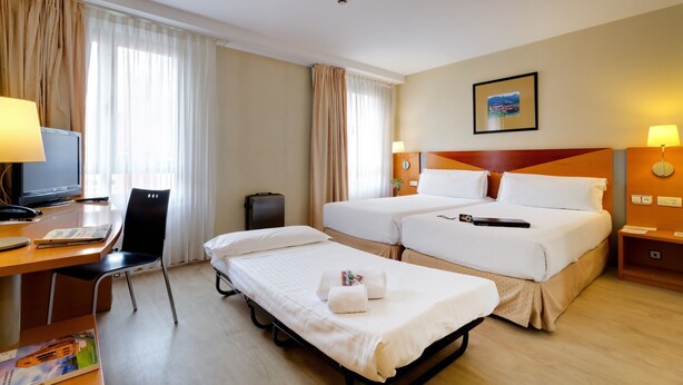 Habitación de hotel con dos camas, un escritorio con computadora, una silla y una mesita de noche con lámpara.