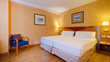 A hotel room with a large bed, a chair, two wall-mounted lamps, and two framed pictures on the walls.