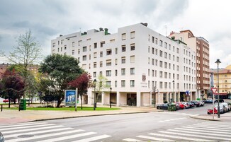 Um hotel com vários andares e fachada moderna, com uma passadeira em frente e carros estacionados na rua.