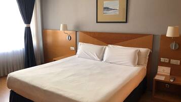 Una habitación de hotel con una cama grande, dos mesitas de noche, una lámpara de pared y un cuadro enmarcado sobre la cama.