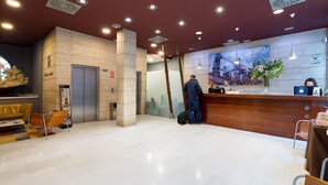 Zona de recepción de un hotel con diseño moderno, que incluye un mostrador, un reloj y una escalera.