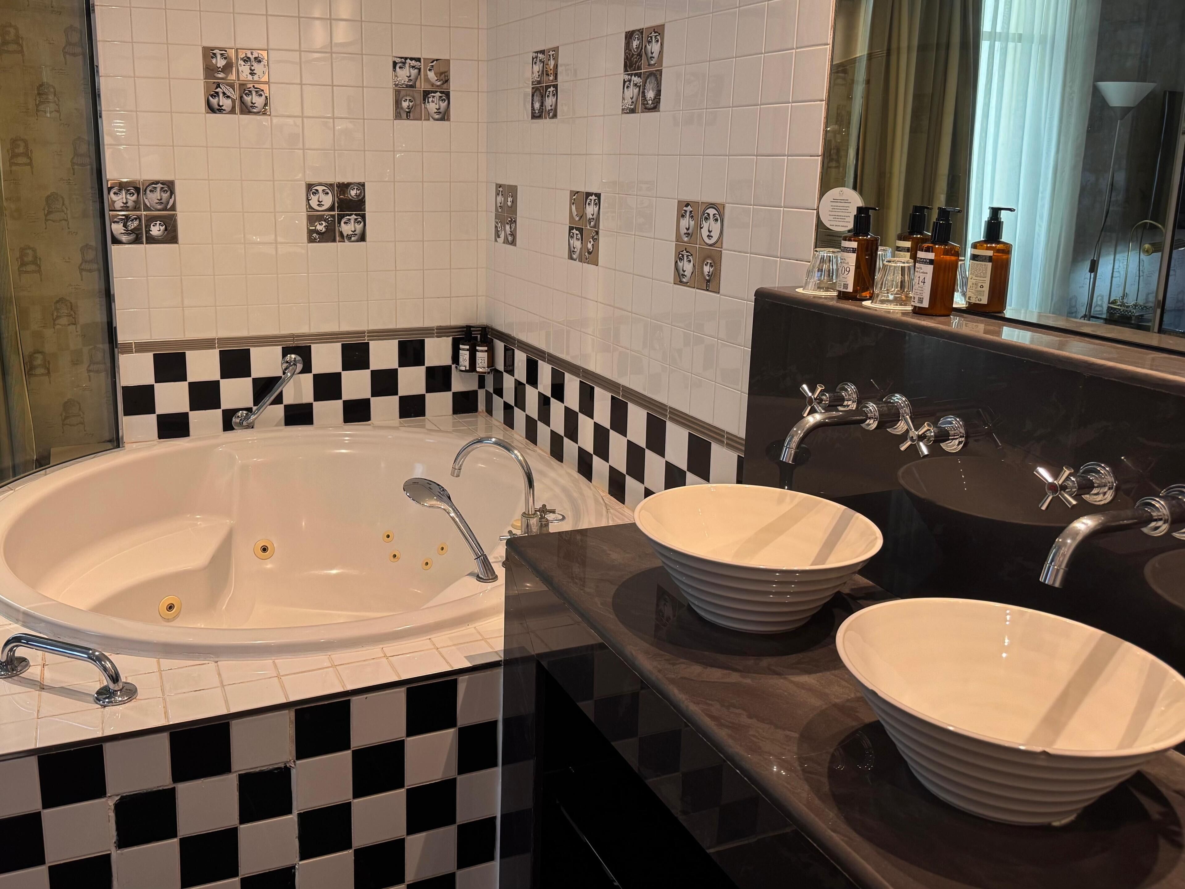 A bathroom with a large bathtub, two sinks with round bowls, and a checkered tile backsplash.