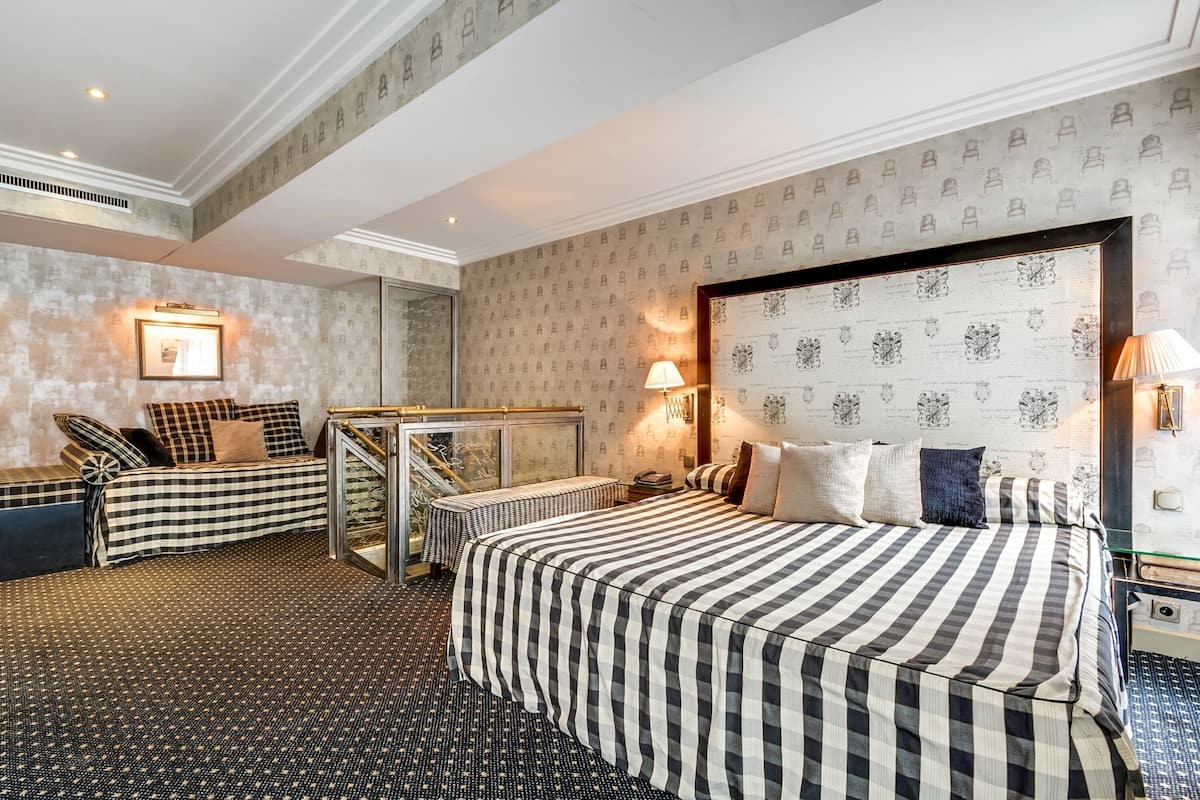 A hotel room with a large bed, a sofa, a small table, and a mirror.