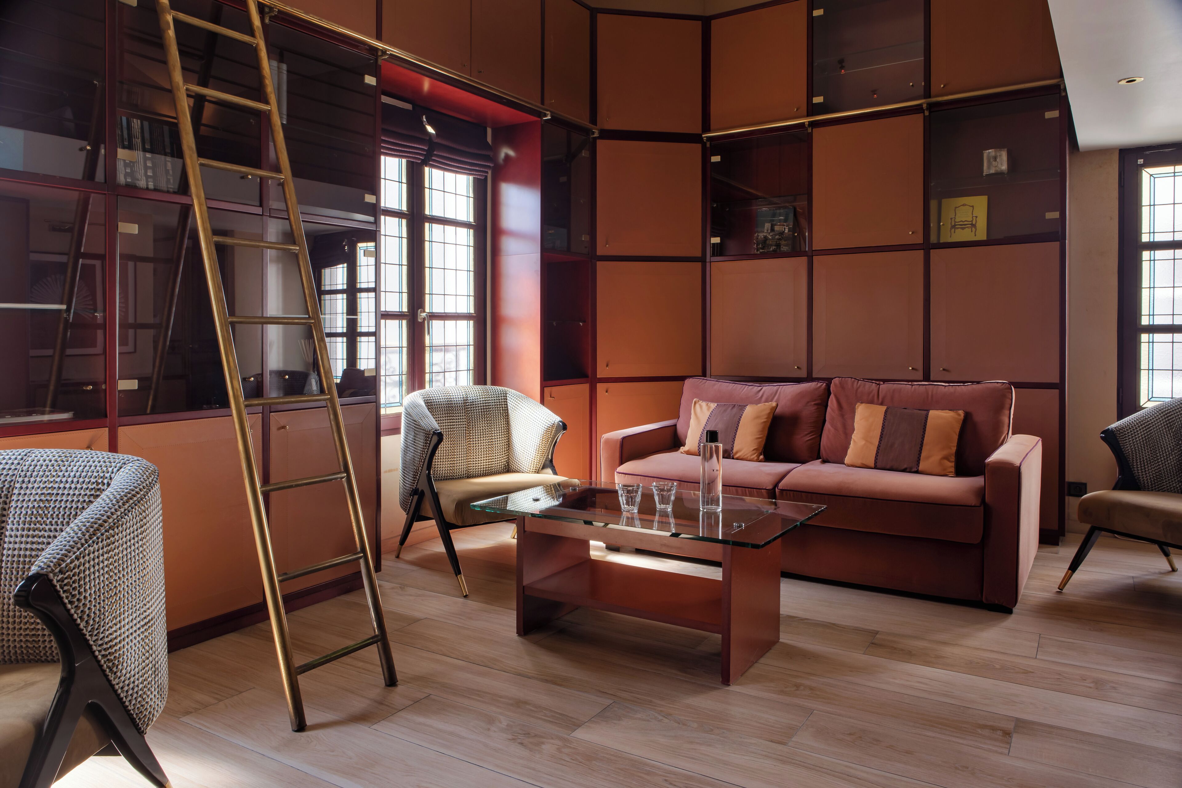 A modern living room with a glass coffee table, a leather sofa, and a ladder against a bookshelf.