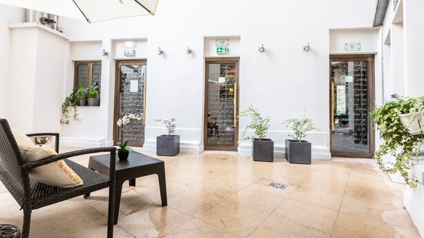 A spacious indoor area with a high ceiling, tiled floor, and several doors leading to rooms. There are potted plants and a wicker chair with cushions. - Villa Lutece Port Royal (Paris)
