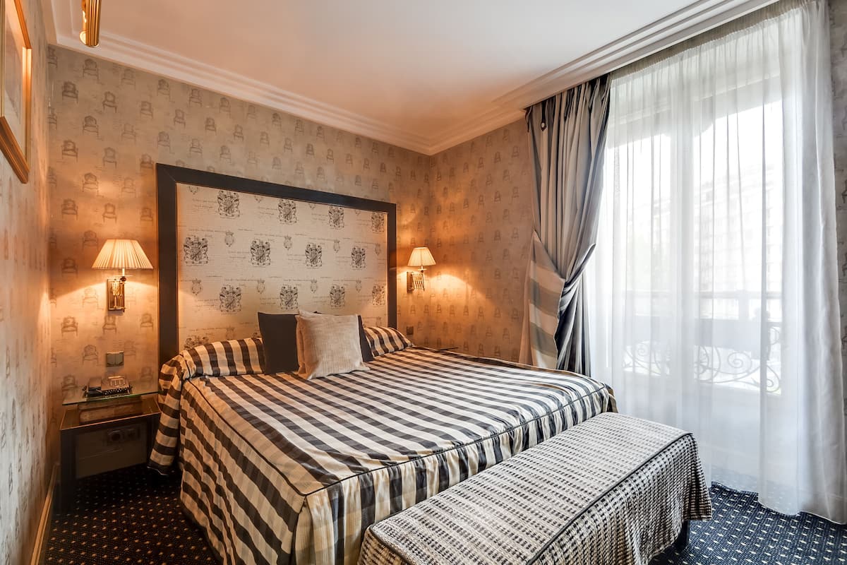 A hotel room with a large bed, a bedside table, a lamp, and a window with curtains.