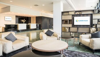 A hotel lobby with seating areas, a reception desk, and a large screen displaying the hotel name.