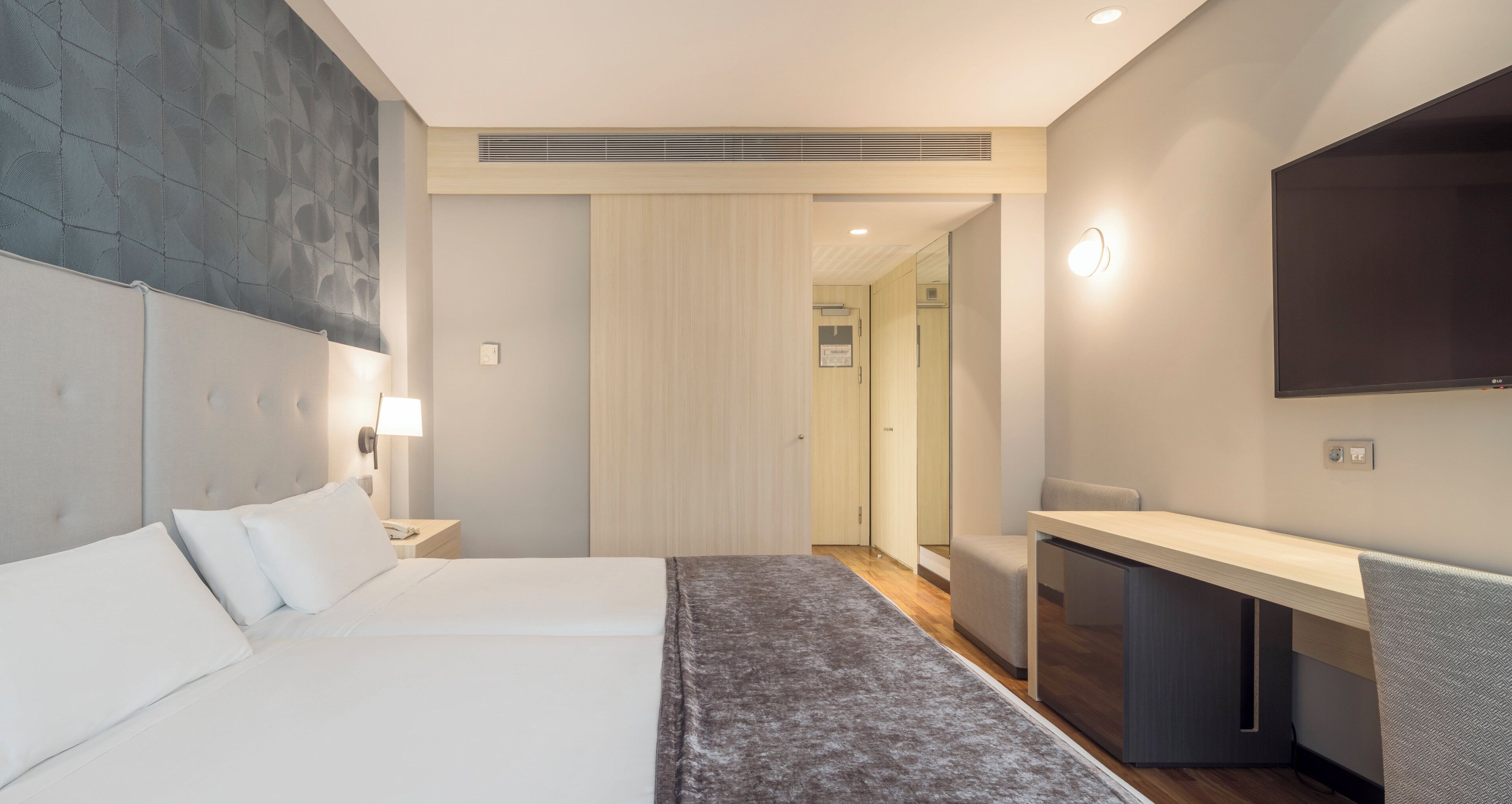 A modern hotel room with a large bed, a desk, and a flat-screen TV.