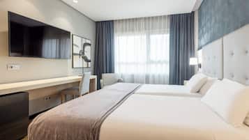 Habitación de hotel con cama, escritorio, silla, televisión y ventana con cortinas.