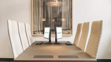 A conference room with a large table, six chairs, two monitors, and a modern pendant light.