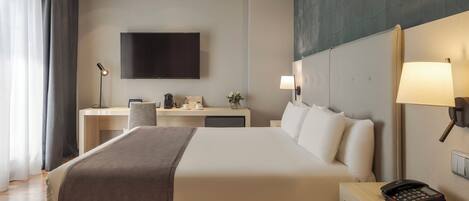 Una habitación de hotel con cama, mesita de noche, escritorio, silla, lámpara y televisor de pantalla plana en la pared.