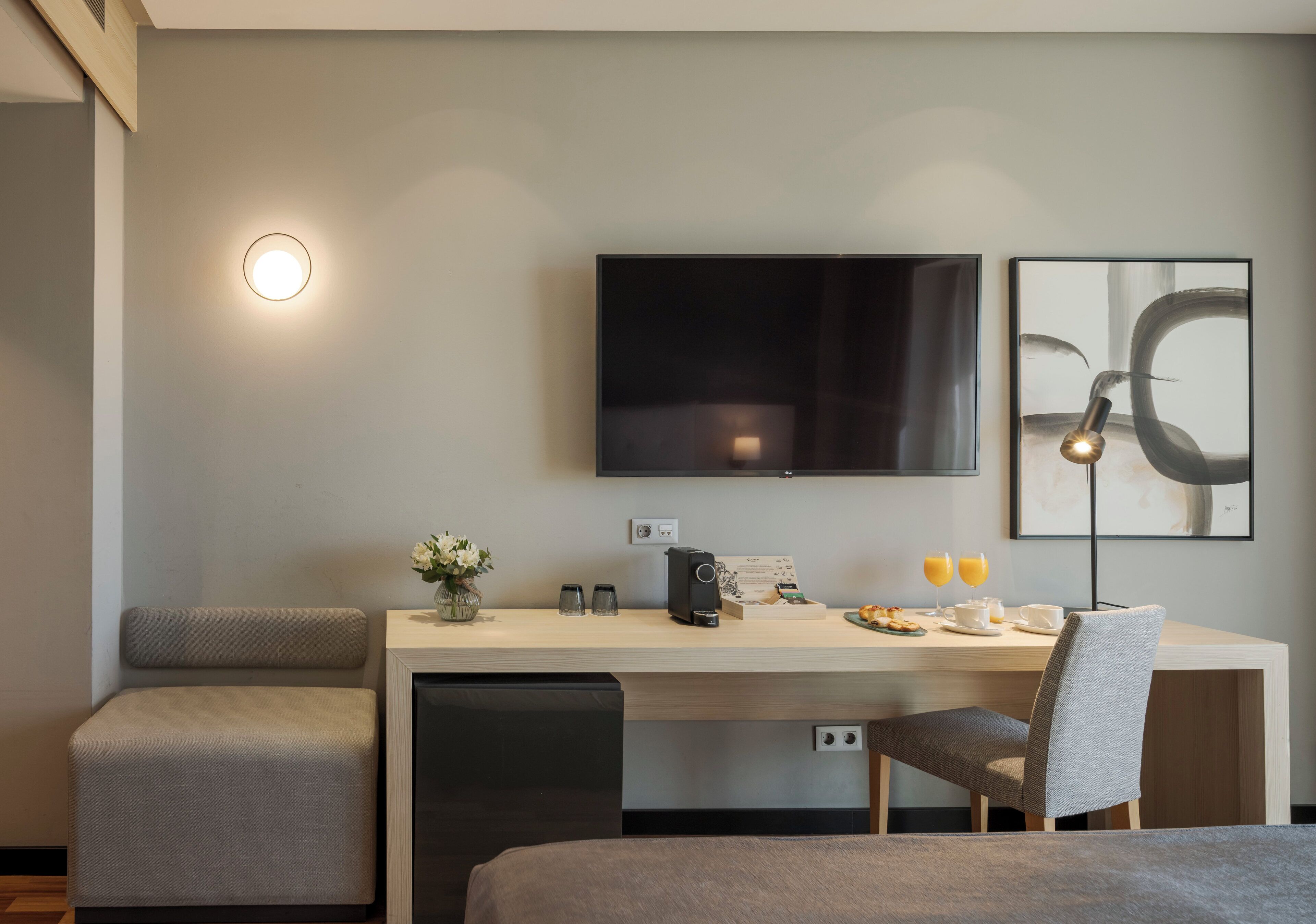 Una habitación de hotel moderna con cama, escritorio con cafetera, televisión y obras de arte en la pared.