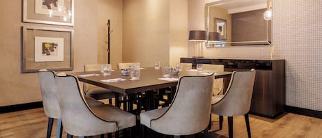 Un comedor moderno con una mesa rectangular, seis sillas y una zona de cocina con un espejo grande y lámparas colgantes.