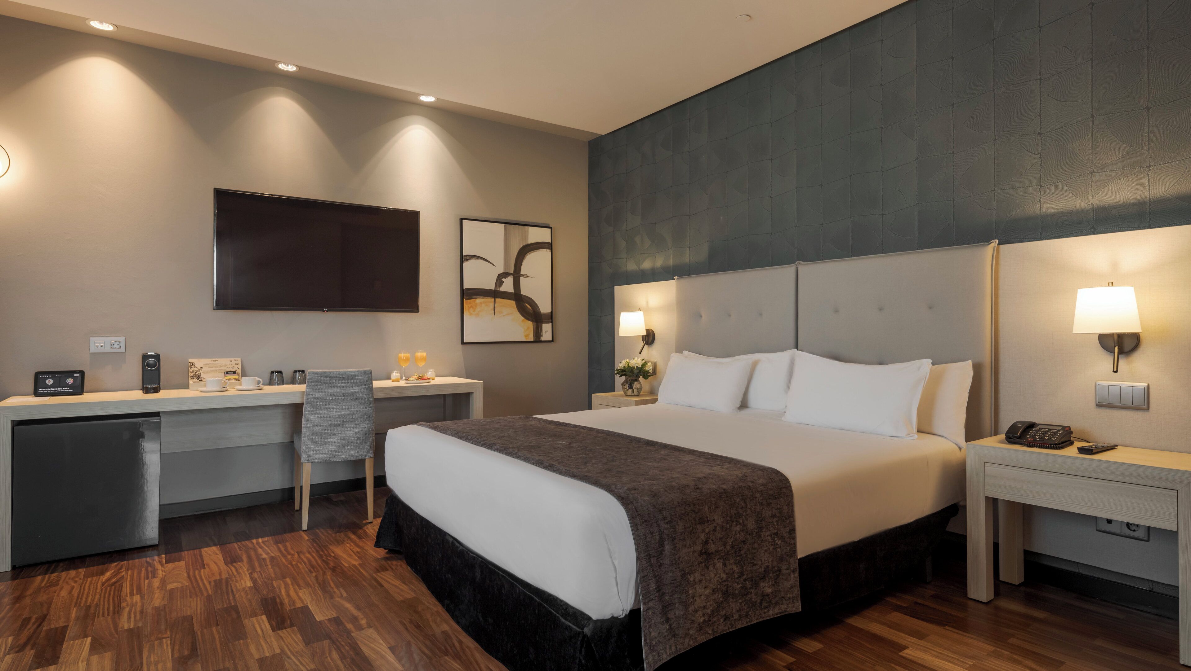 A hotel room with a bed, desk, chair, and a flat-screen TV.