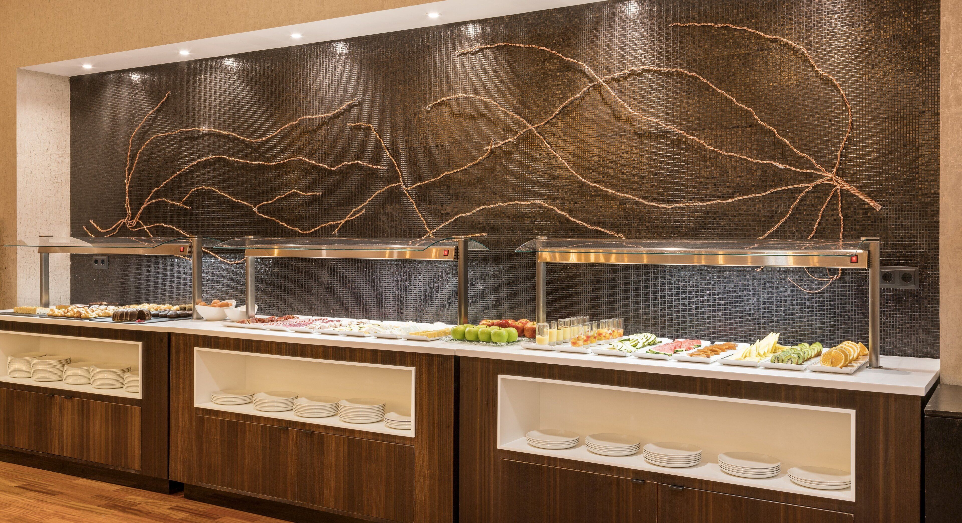 A buffet setup with various food items and a decorative wall with abstract designs.