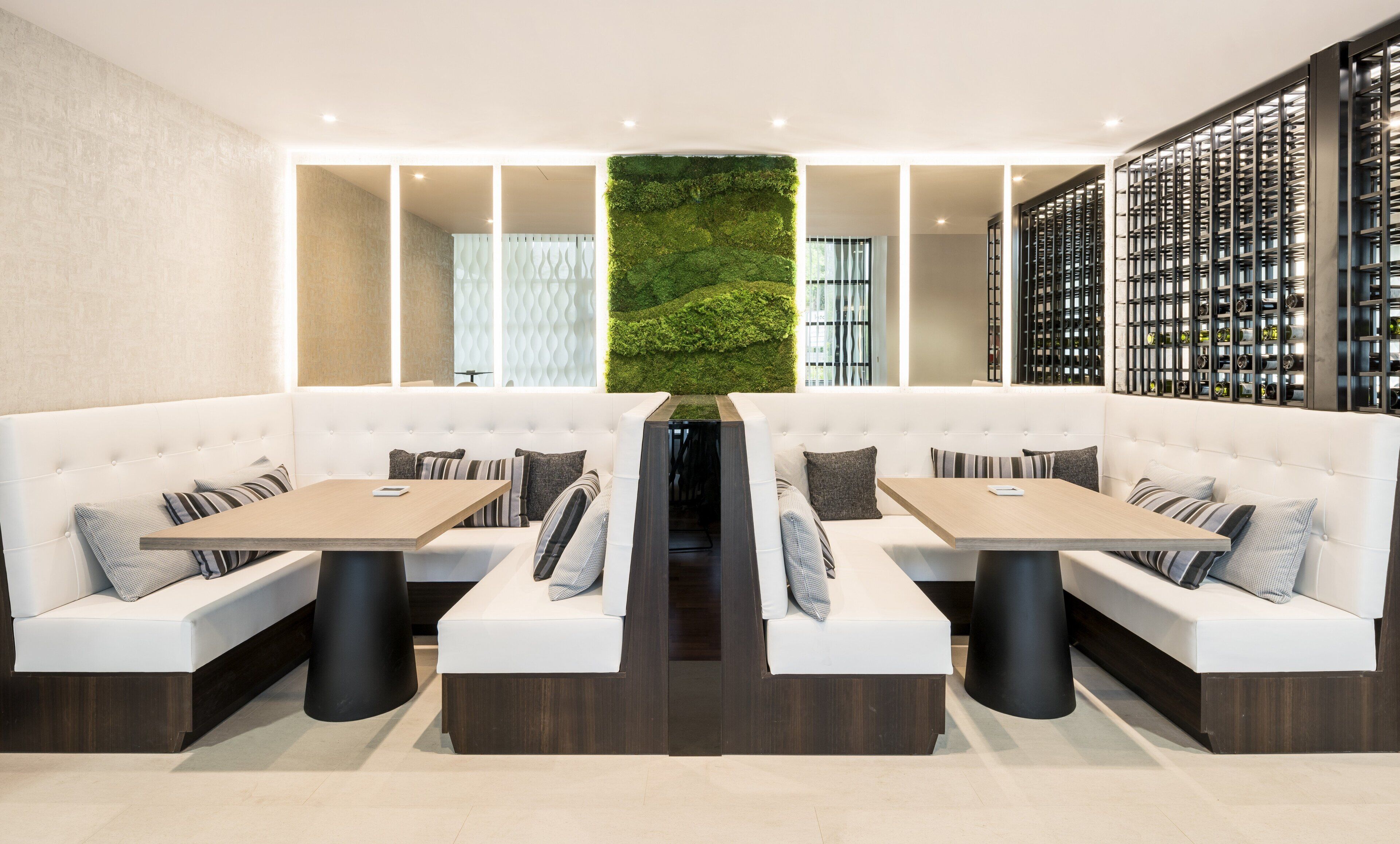 Een modern restaurant met wit beklede zittingen, houten tafels en een groene verticale geveltuin.