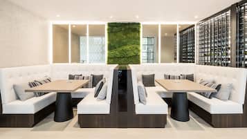 Un restaurante moderno con asientos acolchados blancos, mesas de madera y una pared vertical con jardín.