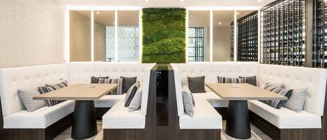 Un restaurante moderno con asientos acolchados blancos, mesas de madera y una pared vertical con jardín.