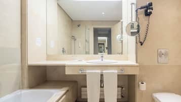 A modern bathroom with a bathtub, a sink, and a toilet. There is a towel rack with two towels, a hairdryer, and a mirror.