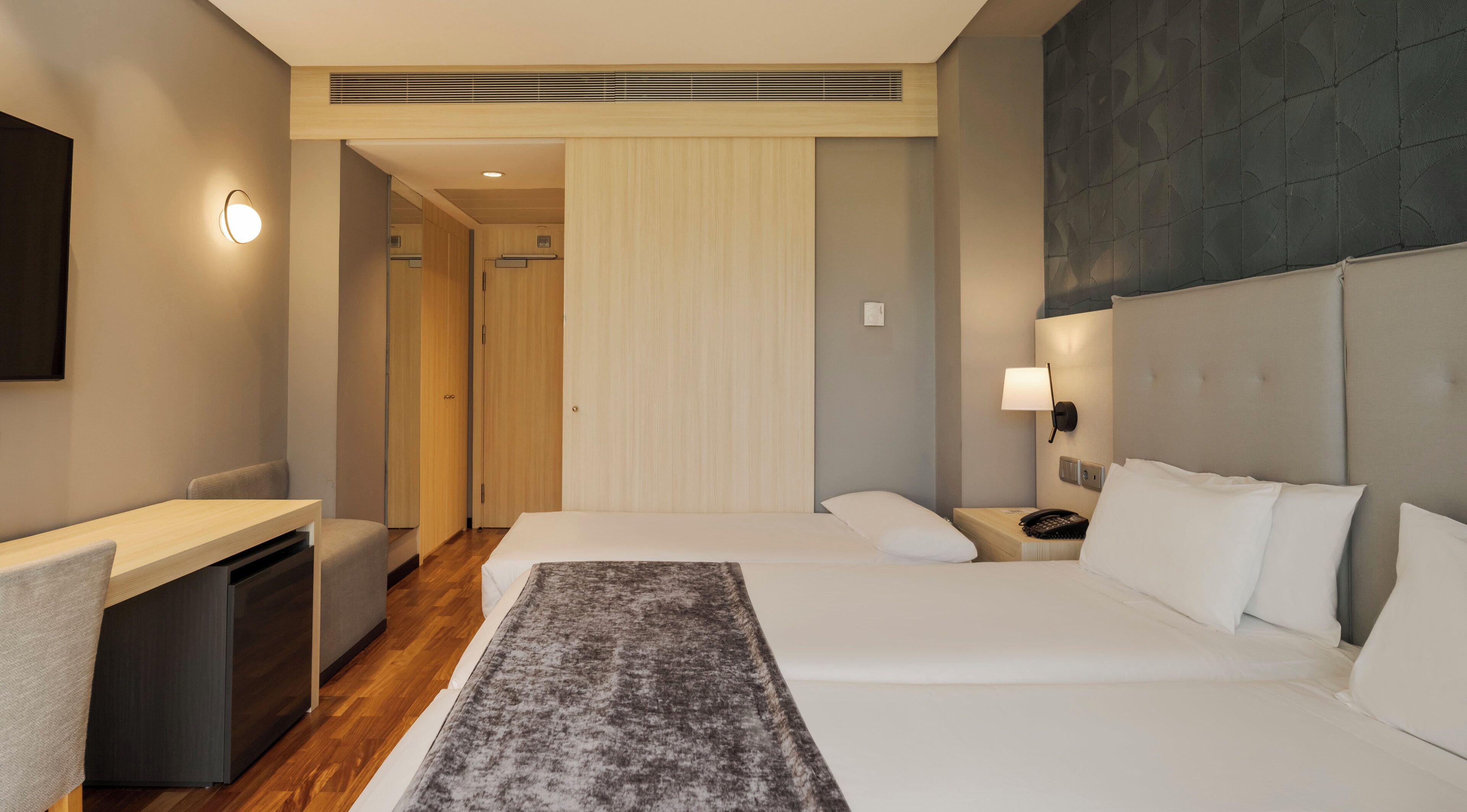 Een hotelkamer met een bed, nachtkastje, bureau en een zithoek.