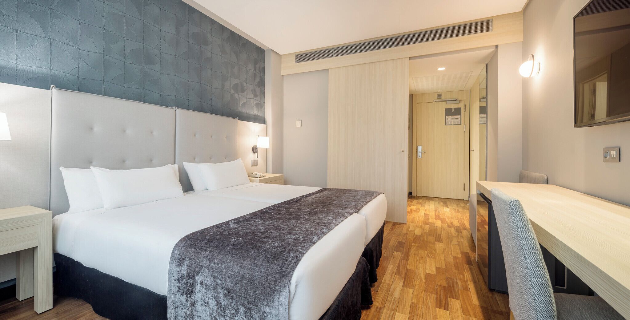 Ein modernes Hotelzimmer mit einem großen Bett, Nachttischen, einem Schreibtisch und einem Spiegel.