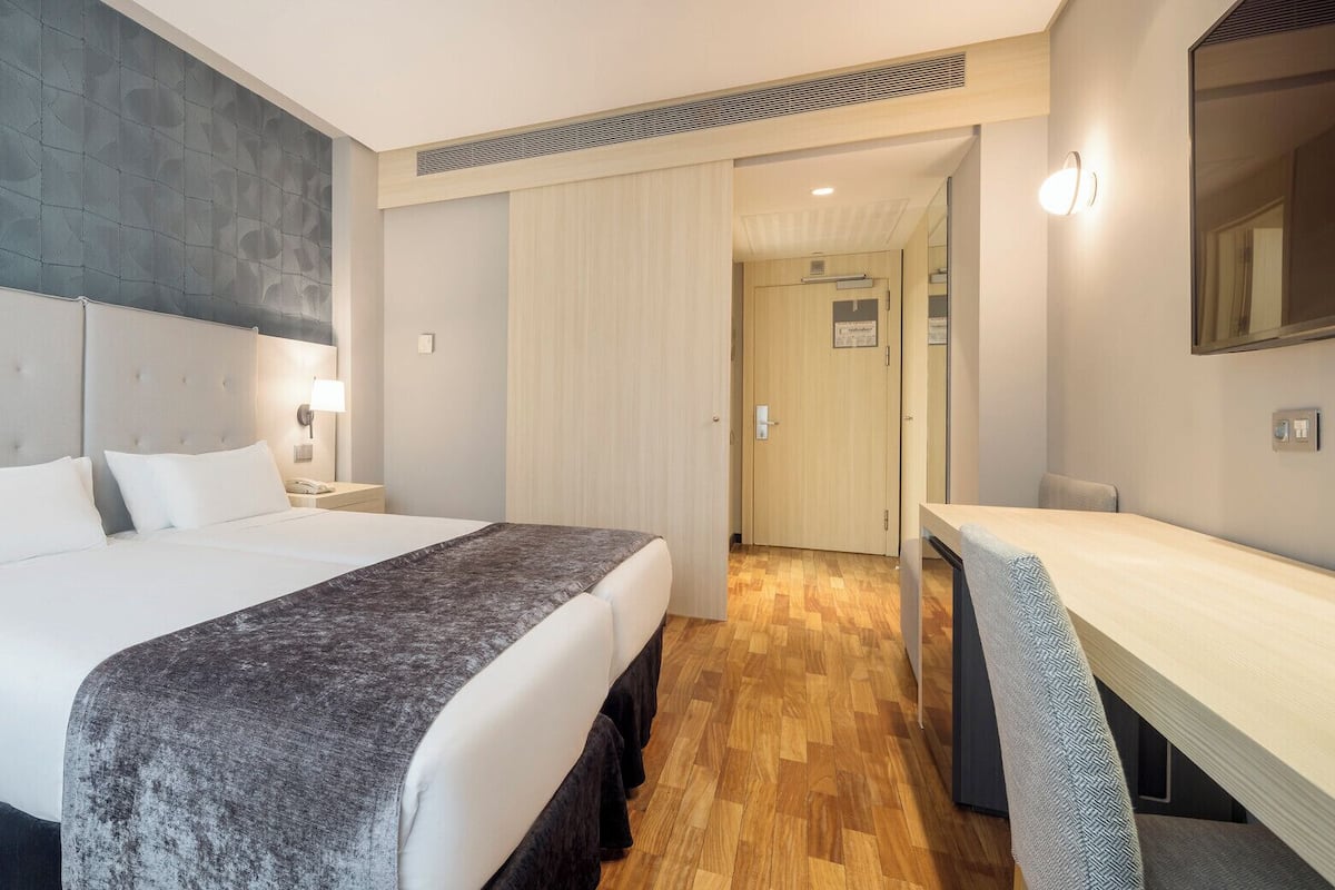A modern hotel room with a large bed, bedside tables, a desk, and a mirror.