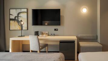 A modern hotel room with a bed, a desk with a chair, a television, and a small kitchenette.