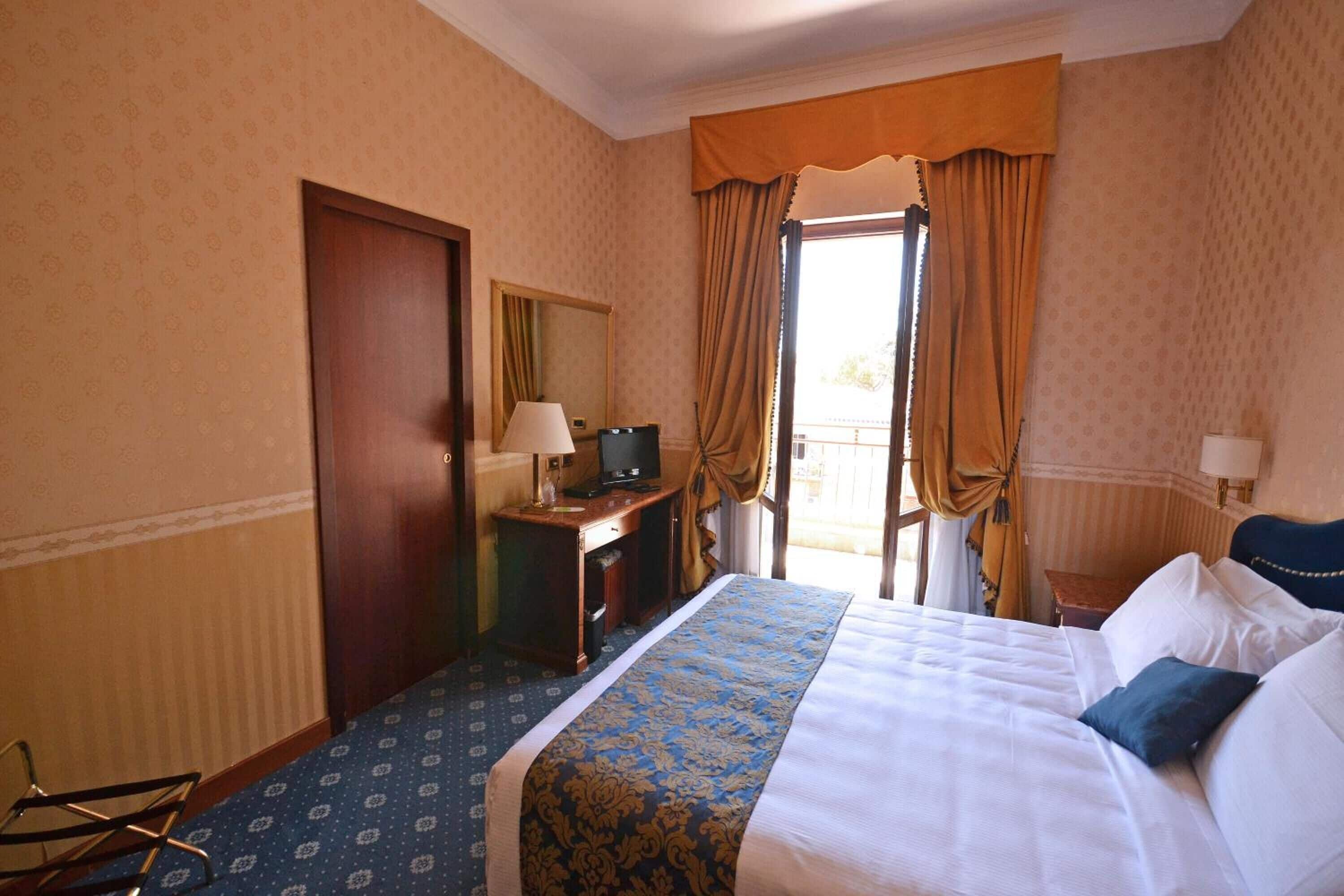 A hotel room with a bed, a desk with a lamp, a television, and a view of the outdoors.
