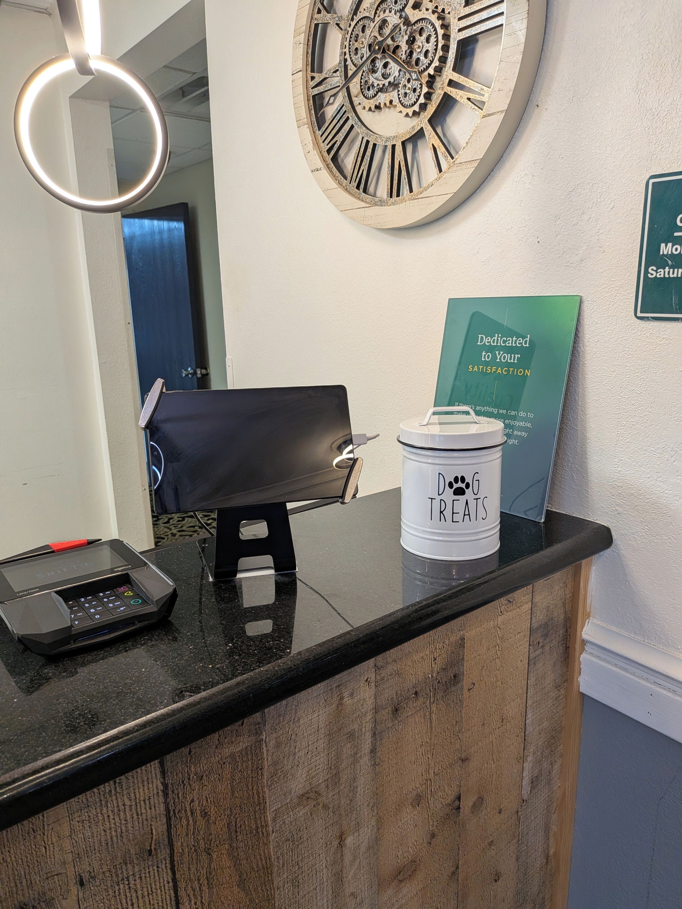 A reception desk with a digital kiosk, a clock, a signboard, and a container labeled 'DOG TREATS'.