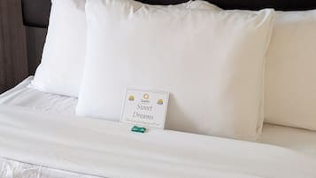 A bed with white bedding and pillows, a dark headboard, and a sign on the pillow.