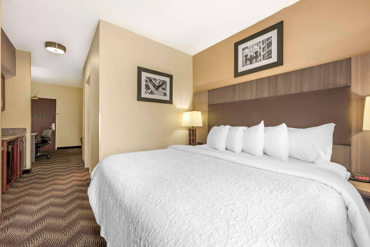 A hotel room with a large bed, a desk with a chair, a lamp, and framed pictures on the walls.