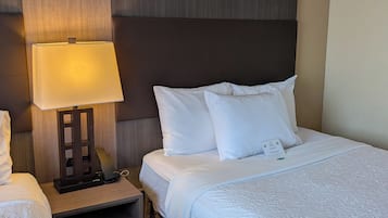 Una habitación de hotel con cama, mesita de noche con lámpara y una pequeña señal sobre el almohadón.