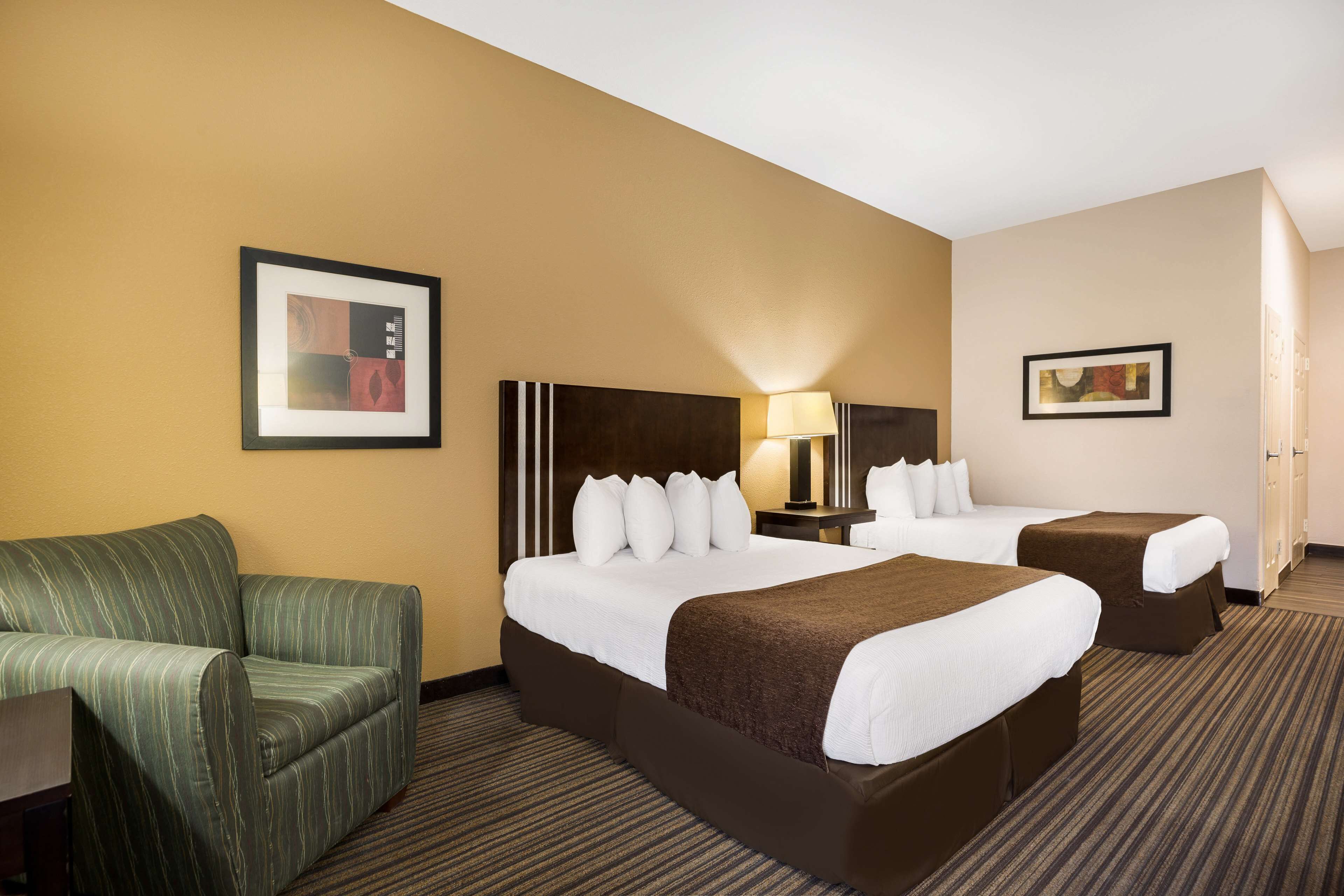 A hotel room with two beds, a sofa, a desk, and framed artwork on the walls.