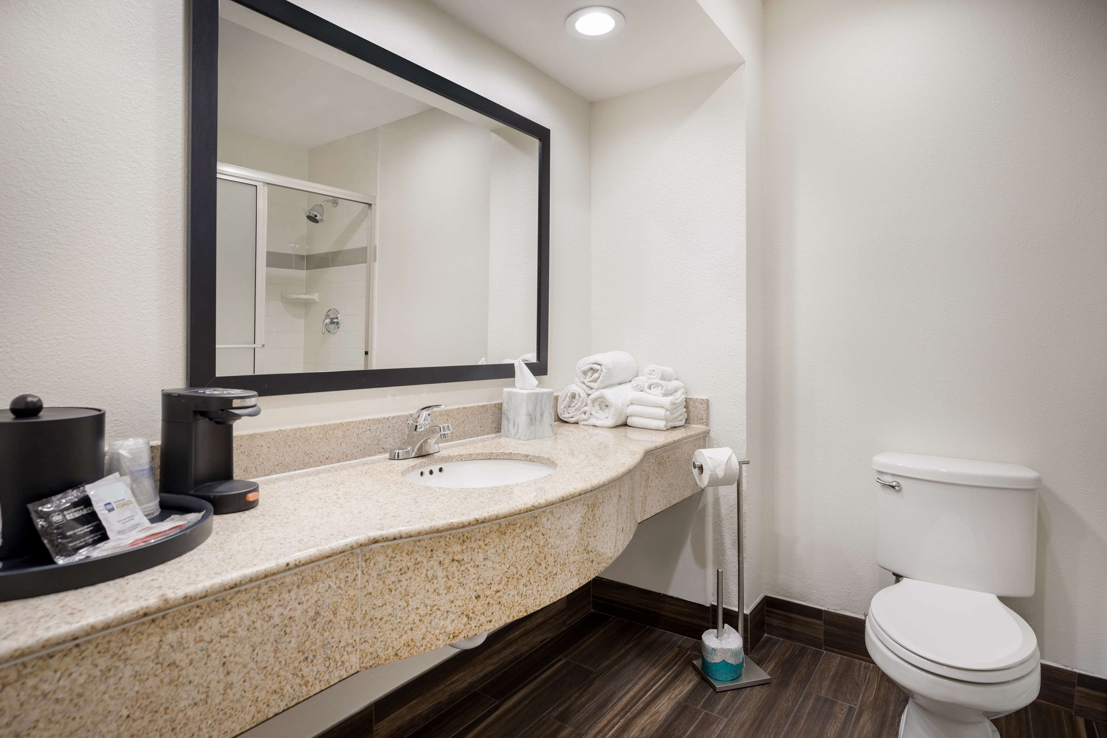 Une salle de bain d’hôtel avec un comptoir en granit, deux lavabos, un grand miroir, des toilettes et un porte-serviettes avec des serviettes pliées.