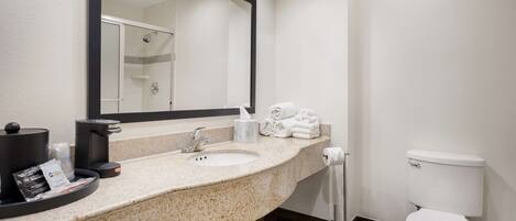 Une salle de bain d’hôtel avec un comptoir en granit, deux lavabos, un grand miroir, des toilettes et un porte-serviettes avec des serviettes pliées.