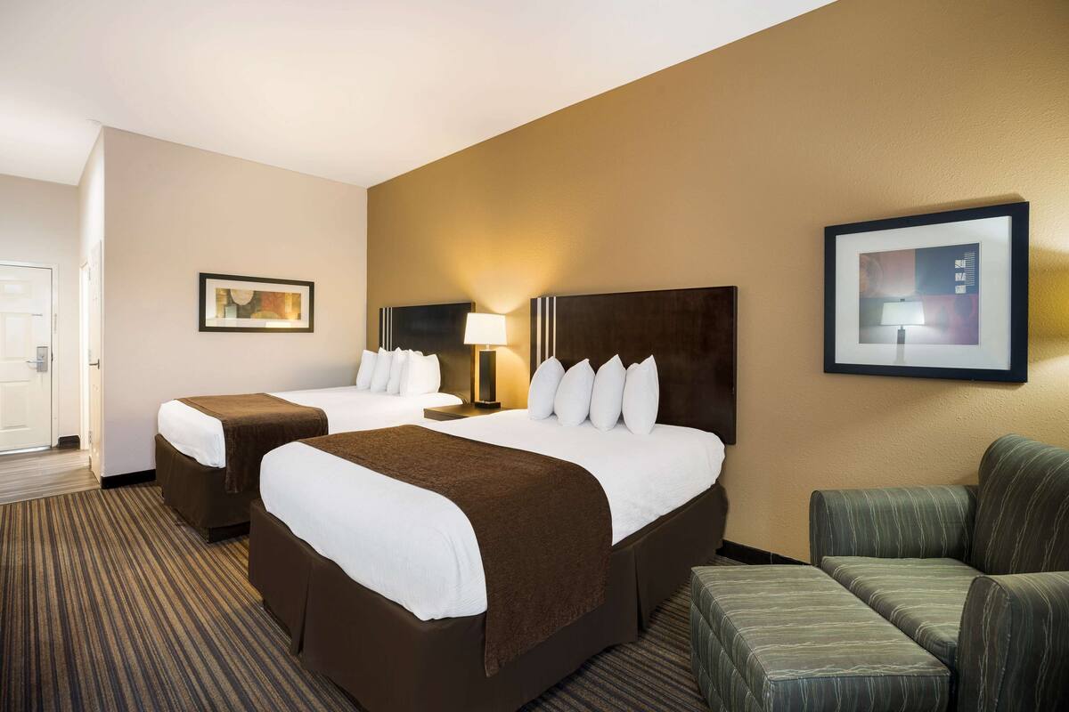 A hotel room with two beds, a sofa, a lamp, and a framed picture on the wall.