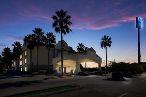 A hotel with a large entrance, palm trees, and a signboard.
