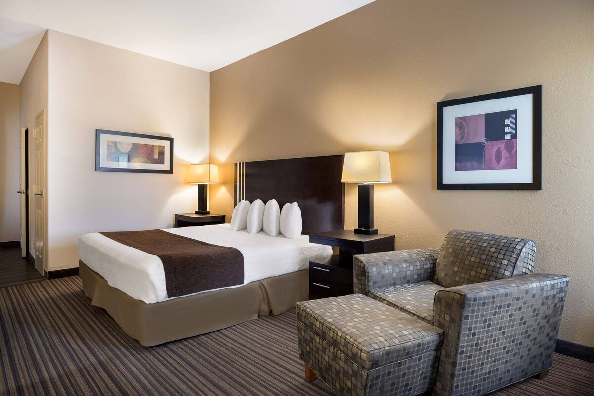 A hotel room with a large bed, two bedside tables with lamps, a chair, and a framed picture on the wall.
