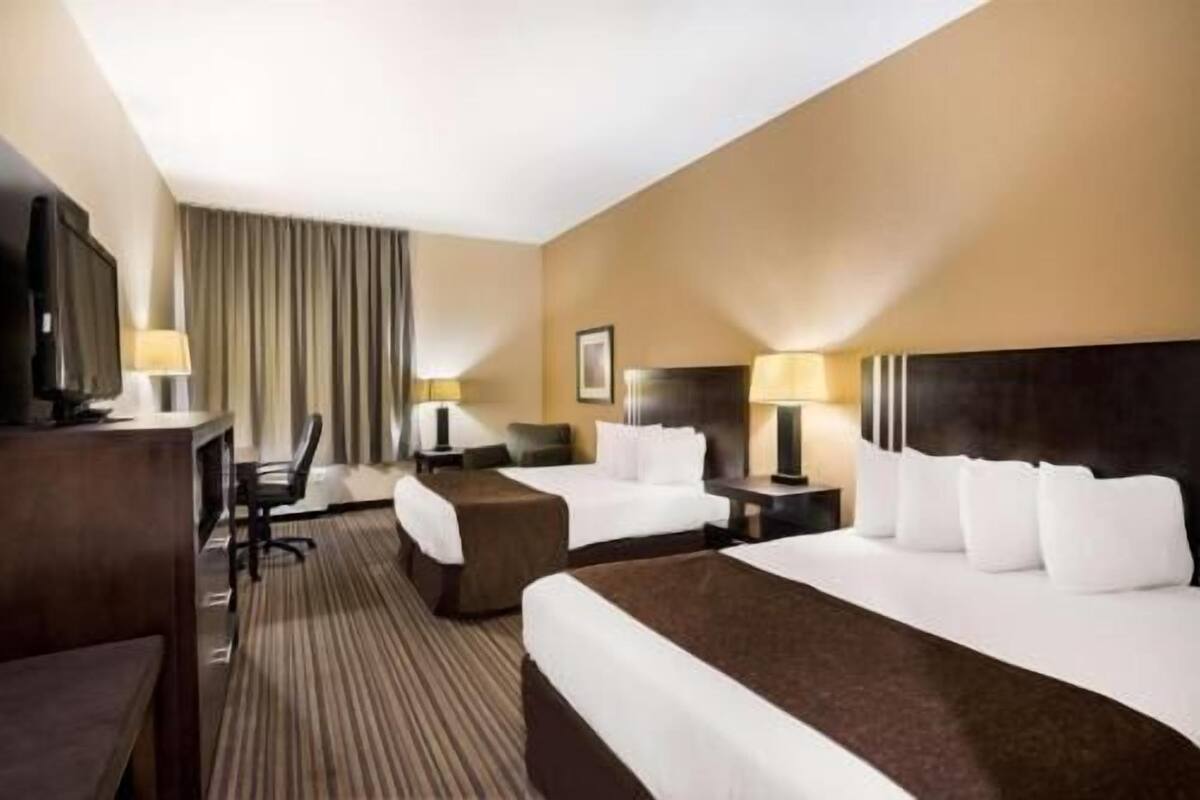 A hotel room with a large bed, two bedside tables with lamps, a desk with a chair, and a television.