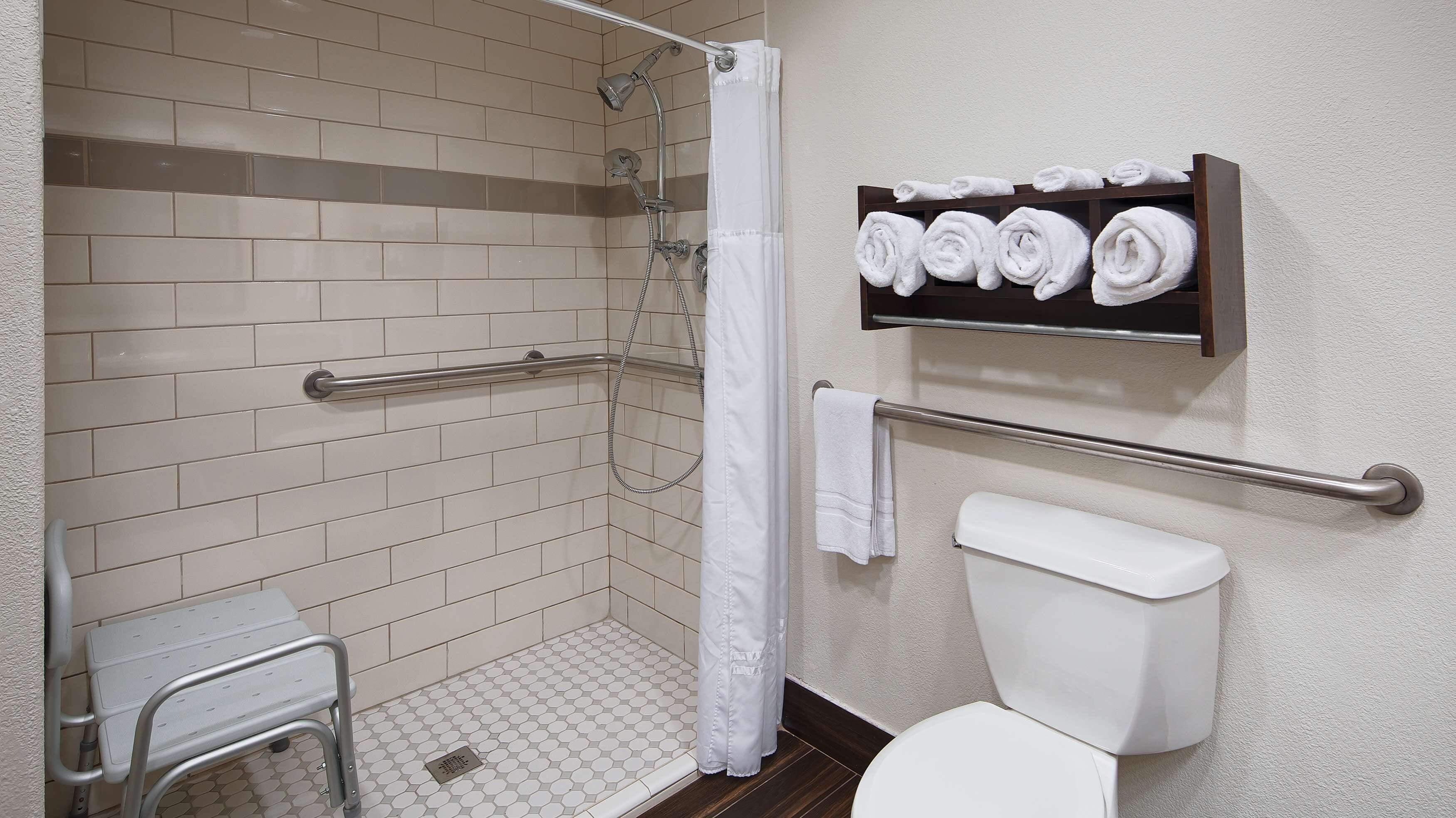 A bathroom with a shower, toilet, and a towel rack with neatly rolled towels.